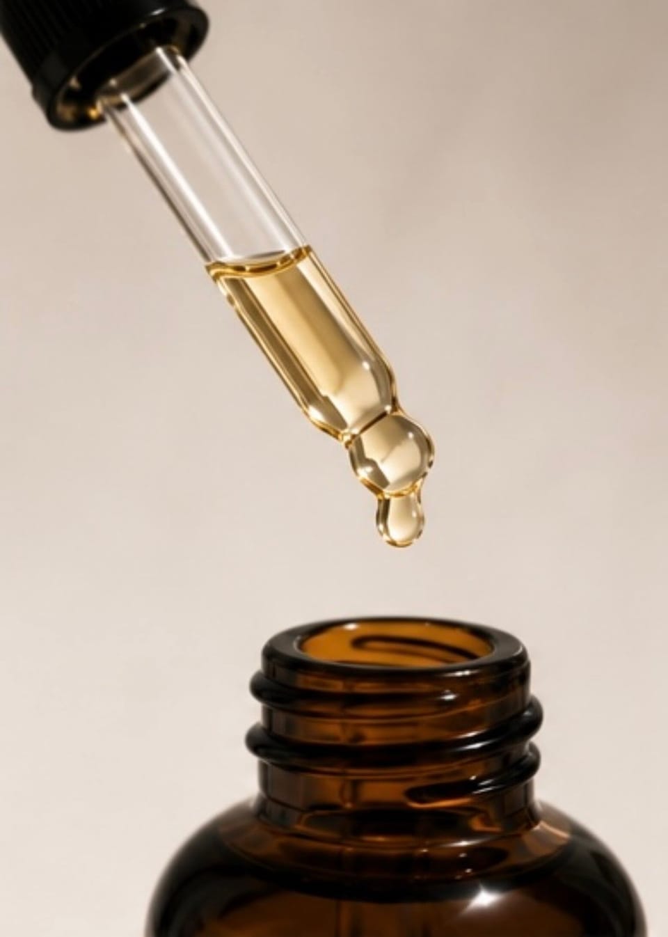 The dropper held above the open bottle, a golden drop of oil falling